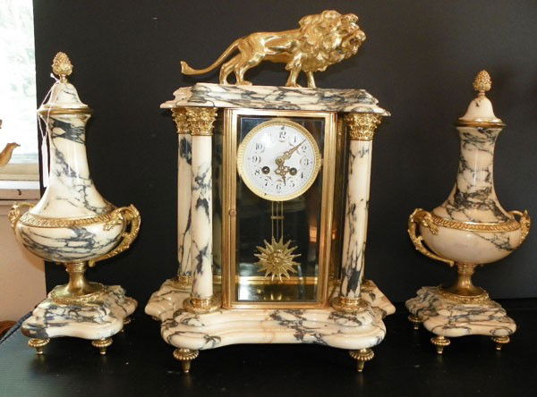 BZ & MBL 3 PC CLOCKSET W/ BZ LION TOP & SIDE URNS: Bronze & being and black marble 3 piece clock set with side urns. The center piece features a bronze lion on top & a pendulum featuring a sun with a lady face in center. Dimensions: Center- 19.5"H x 1