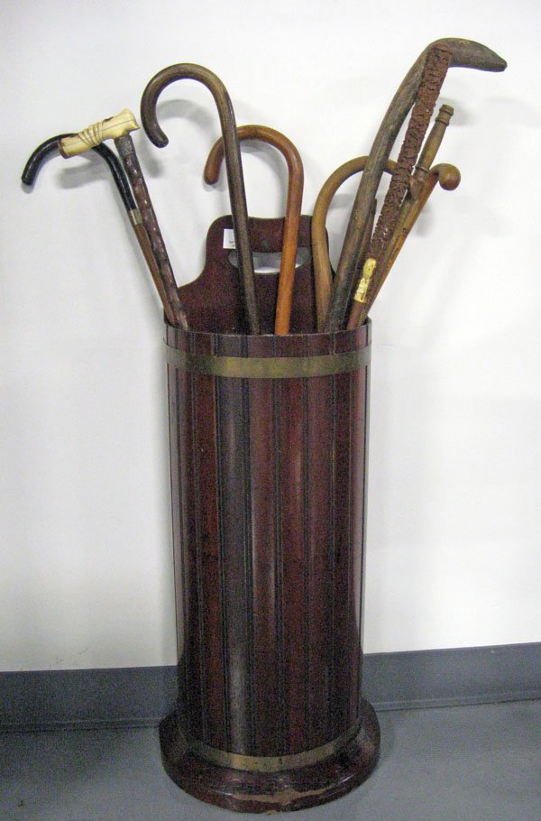 Mahogany umbrella stand and canes. Stand has a ree: Mahogany umbrella stand and canes. Stand has a reeded front, brass bands, and a tin liner. Some wear to wood at base. Ten canes are in as found worn condition. 31''h x 13 1/2''l x 8''d. $100-150