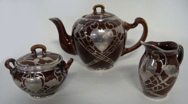 Three piece sterling silver over pottery tea set. Tea p: Three piece sterling silver over pottery tea set. Tea pot, sugar and creamer. Interior rim of the sugars lid is damaged. Appropriate age wear. $80-120