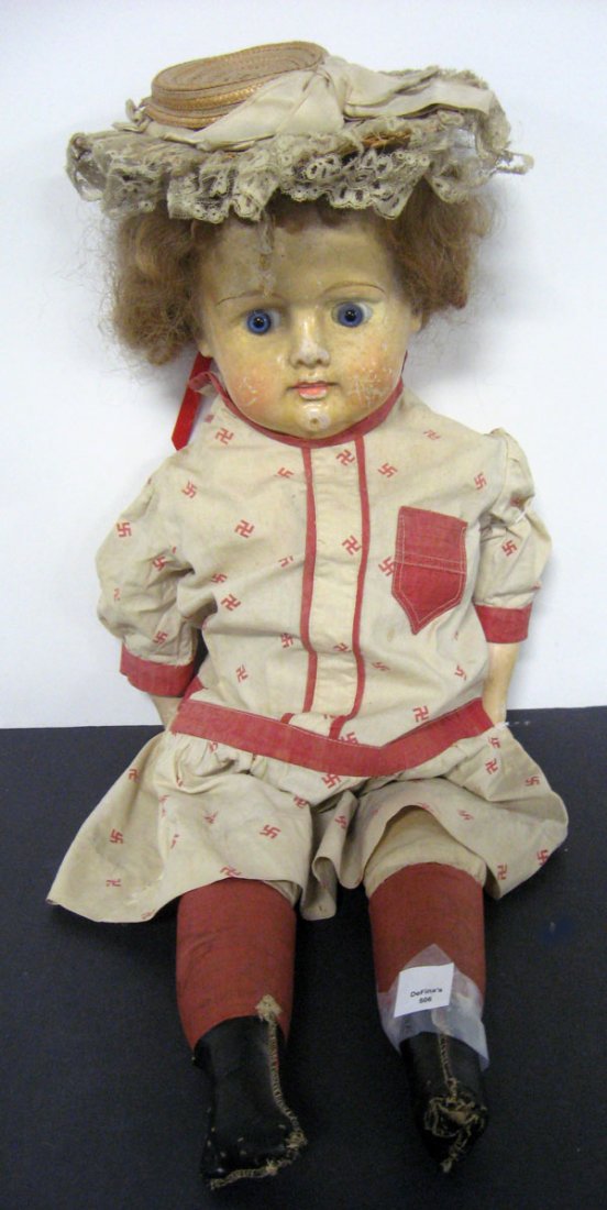 26'' papier mache doll. German with cloth body, papier: 26'' papier mache doll. German with cloth body, papier mache head, glass paperweight set eyes, original wig. Antique swastika dress. Note wear to face, scratches, cloth body leaking [tape to left leg]