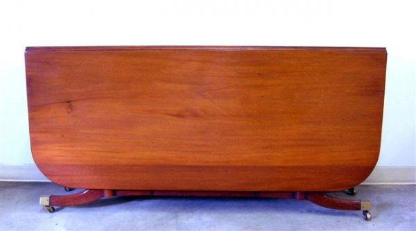 Mahogany drop-leaf table. Ca 1950. Duncan Phyfe: Mahogany drop-leaf table. Ca 1950. Duncan Phyfe extension table, reeded port feet, brass cup casters. Need some minor refinishing to base. Some scratches to table surface. 29''h x 60''w x 18''d.