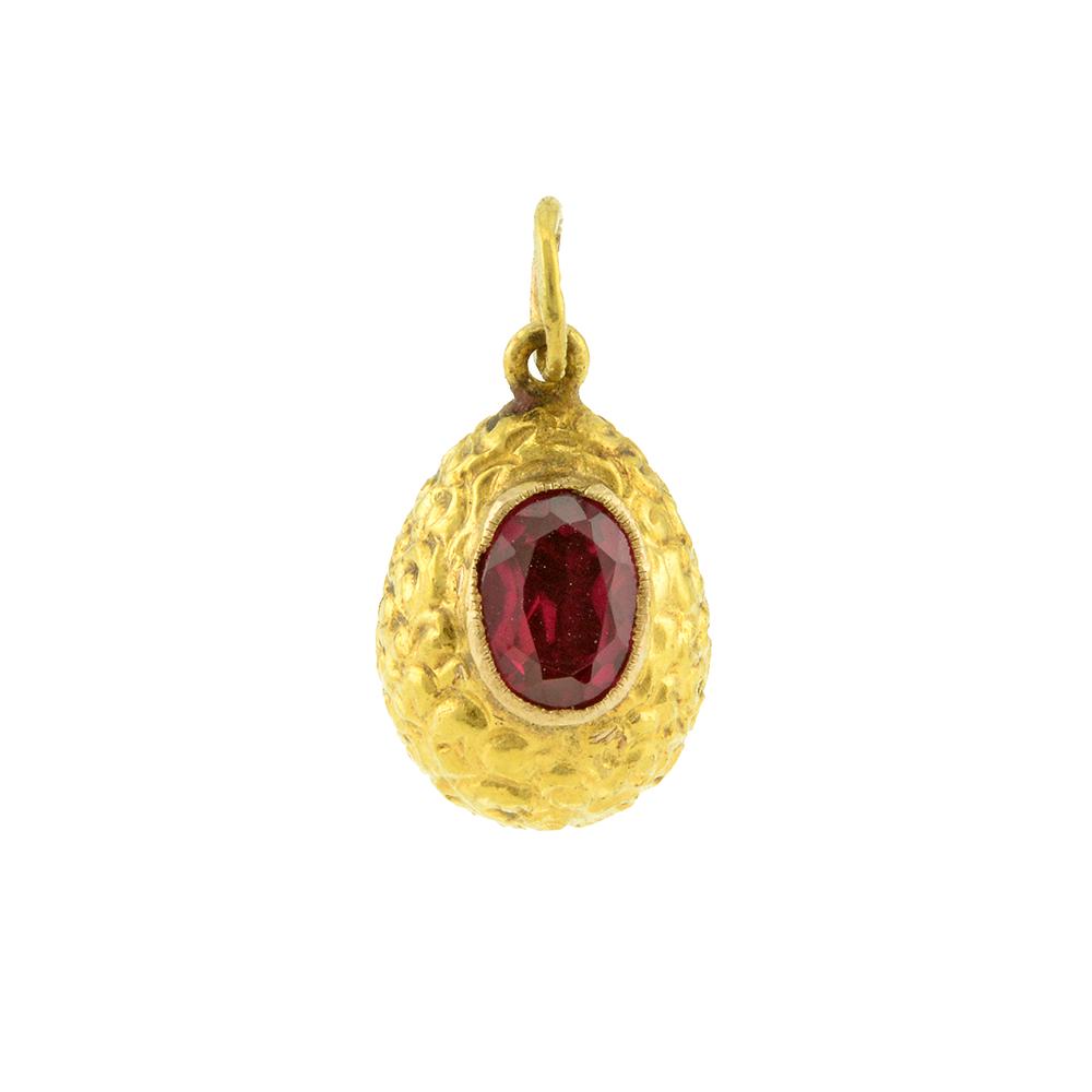 A Russian Gold and Spinel Miniature Pendant Easter Egg: A Russian gold and spinel miniature pendant Easter egg, illegibly marked, circa 1900. The chased gold body decorated with scrolls and set with a magenta cabochon spinel. Height: 5/8 in.