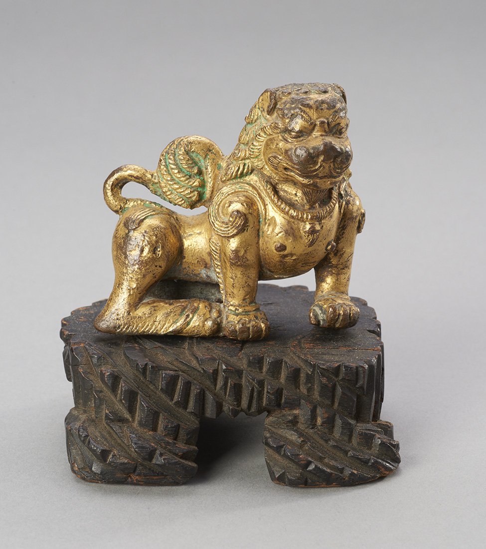 Ancient Nepalese Gilt Copper Lion: Nepal, ca. 13th century. The fierce protective beast with well-defined mane and tail. Custom base. MEASUREMENTS Height: 2 3/4 inches long / 7 cm