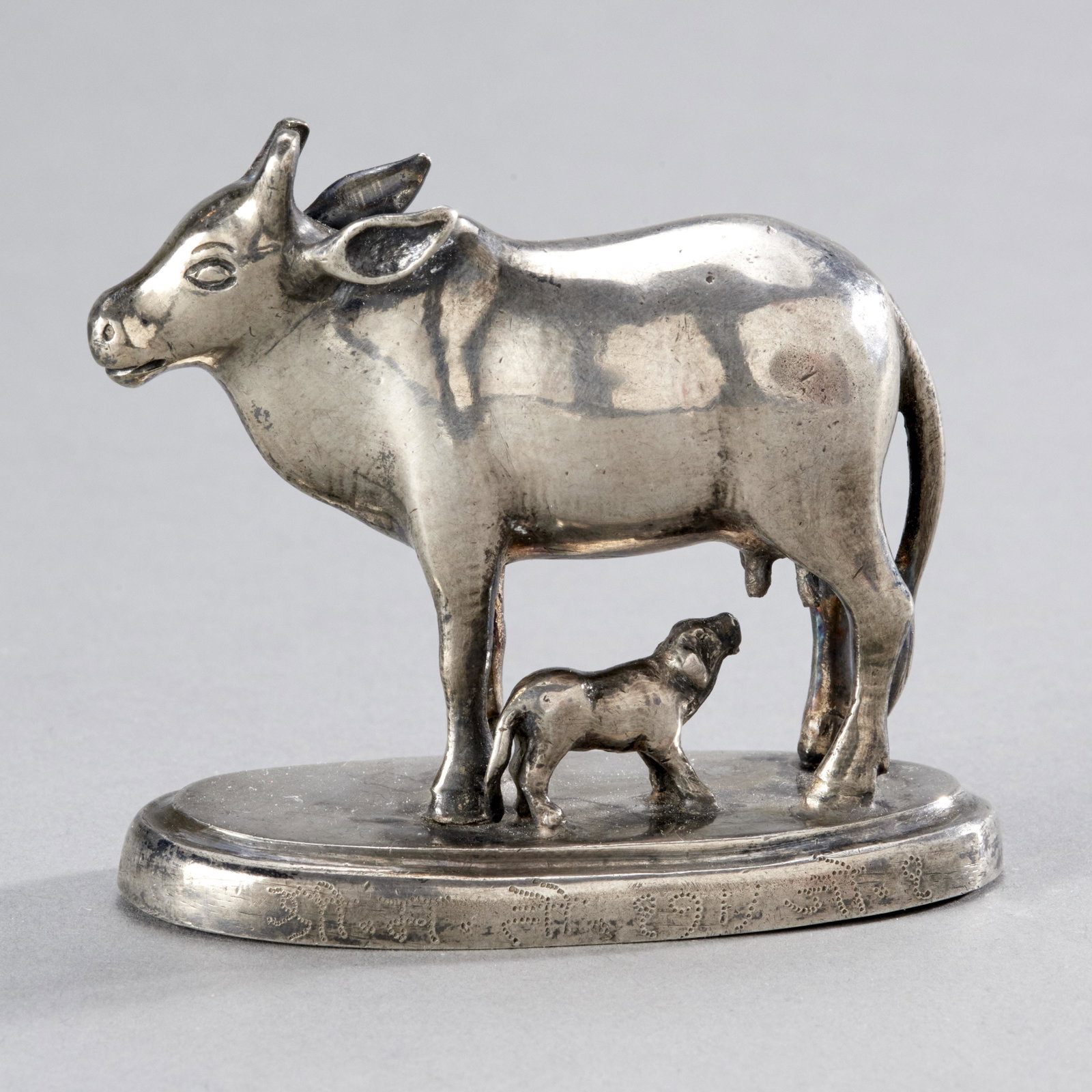 Indian Silver Nursing Cow: India, ca. 19th century. Charming depiction of a cow suckling its calf, the base with inscription and possible date. Ex: Doris Wiener Collection. MEASUREMENTS 2 1/2 inches tall / 6.3 cm SHIPPING $20 f
