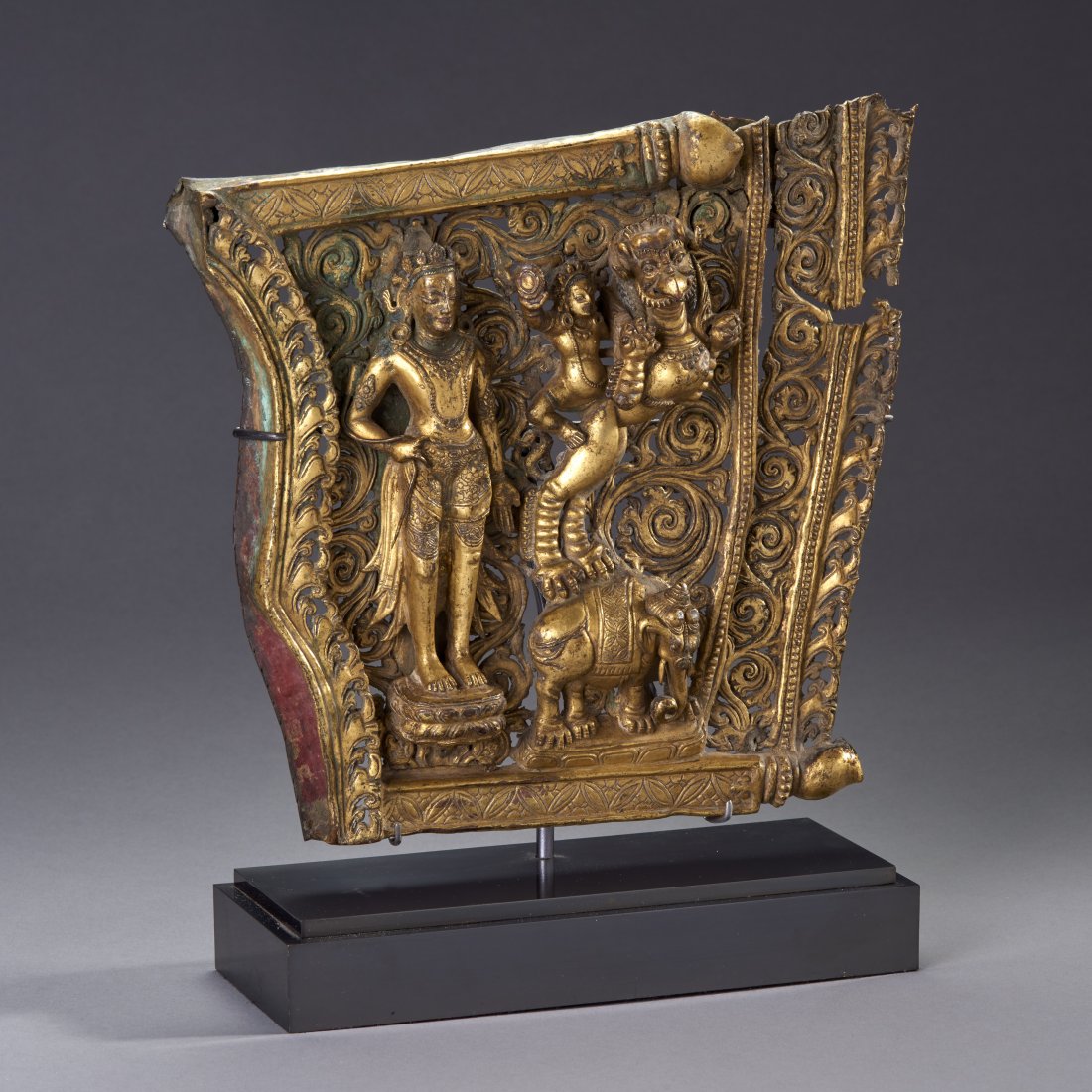Fine Nepalese gilt bronze plaque: Nepal, ca. 15th - 16th century. A very fine openwork fragment from a Torana featuring a deity riding a griffin which is itself riding an elephant, adjacent to a large, seperately cast figure of a stan