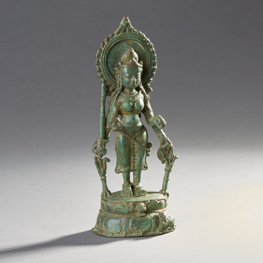 A Pala Bronze Female Deity: North India, ca. 8th-9th century. An early Pala depiction, likely of Parvati holding sword and shield standing atop a tiered base, a small figure of a lion below. Height: 7.8 inches / 19.7 cm