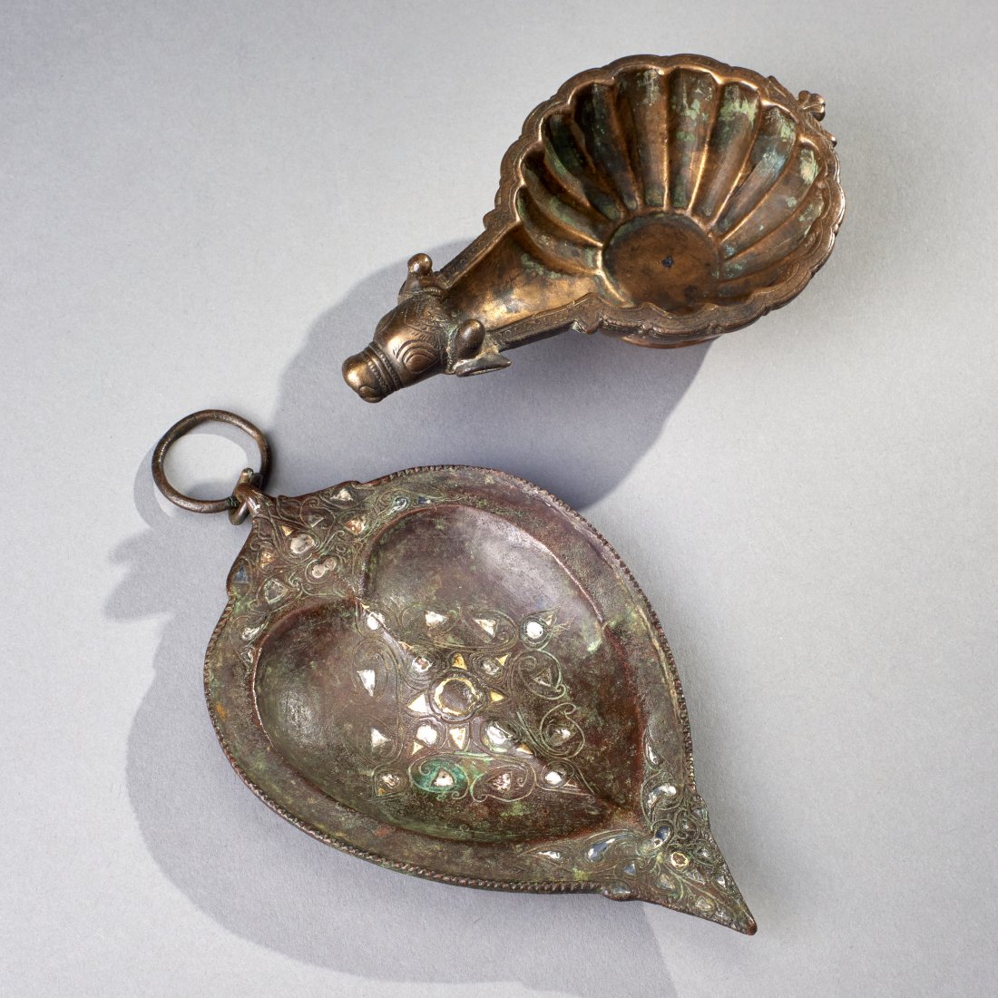 Two Indian and Himalayan Bronze Lamps: India and Nepal, ca. 18th-19th century. Two bronze ritual lamps, the large example likely Himalayan and with silver and electrum(?) inlay, the smaller example is Indian with Nandi Bull spout. Length o