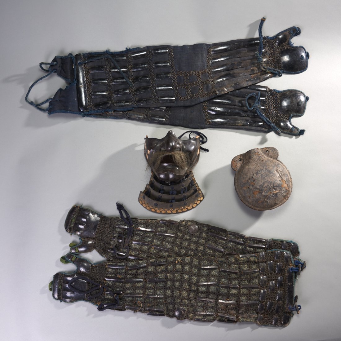 Six Pieces of Japanese Armor: Japan, ca. Edo Period. Six pieces of armor, consisting of two sets of arm defenses, each of sleeve form and encased in steel chains and plates, both terminating in hand protectors, a composition Menpo