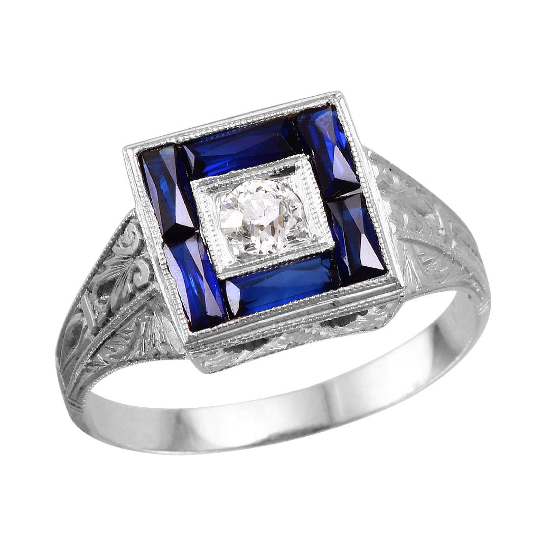 20KT White Gold Antique Vintage Synthetic Sapphire: This square shaped men's ring is designed in brightly polished 20KT white gold, and contains one round brilliant cut diamond in the center. Baguette cut sapphires are invisibly channel set all the way