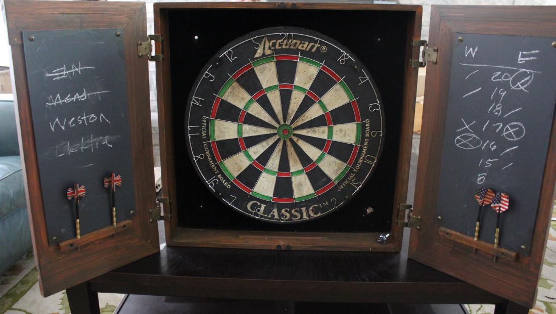 Accuart Classic Dart Board in Cabinet: Accuart Classic Standard English Dart Board in a two door cherrywood cabinet. With USA and English flag embellished darts. Two door cabinet has fitted interior (darts not complete) 22"h. x 22"W. x 4"D