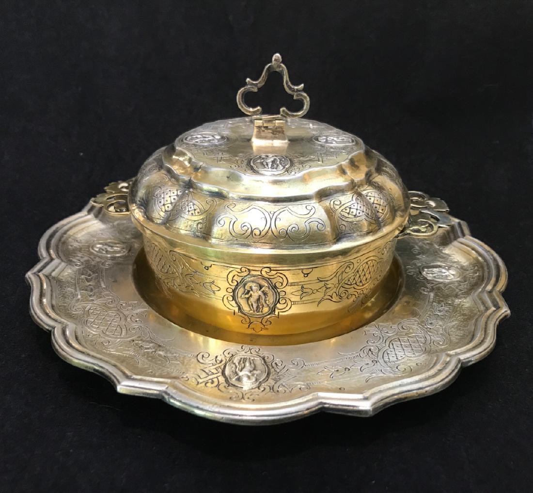 18th C Augsburg Silver-Gilt Covered Ecuelle and: German Augsburg Etched silver-gilt two handled covered ecuelle decorated with repousse winged cherub medallions and etching on a scalloped edge underplate with same decorations. Vermeil interior. Zig-