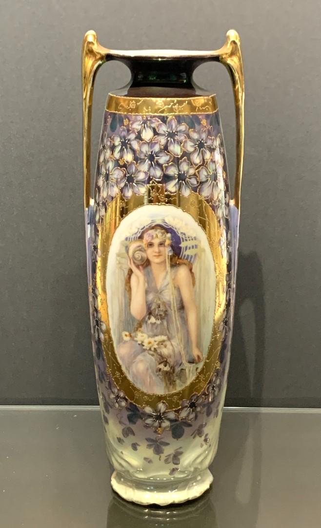 German Hand Painted Porcelain Portrait Vase: Hand painted porcelain vase. Art Nouveau design. Depicting a seated maiden holding a conch shell draped with waterlilies. Floral lustre and gilt decoration. Marked at the underside; 12.25in.H. x 4in.W