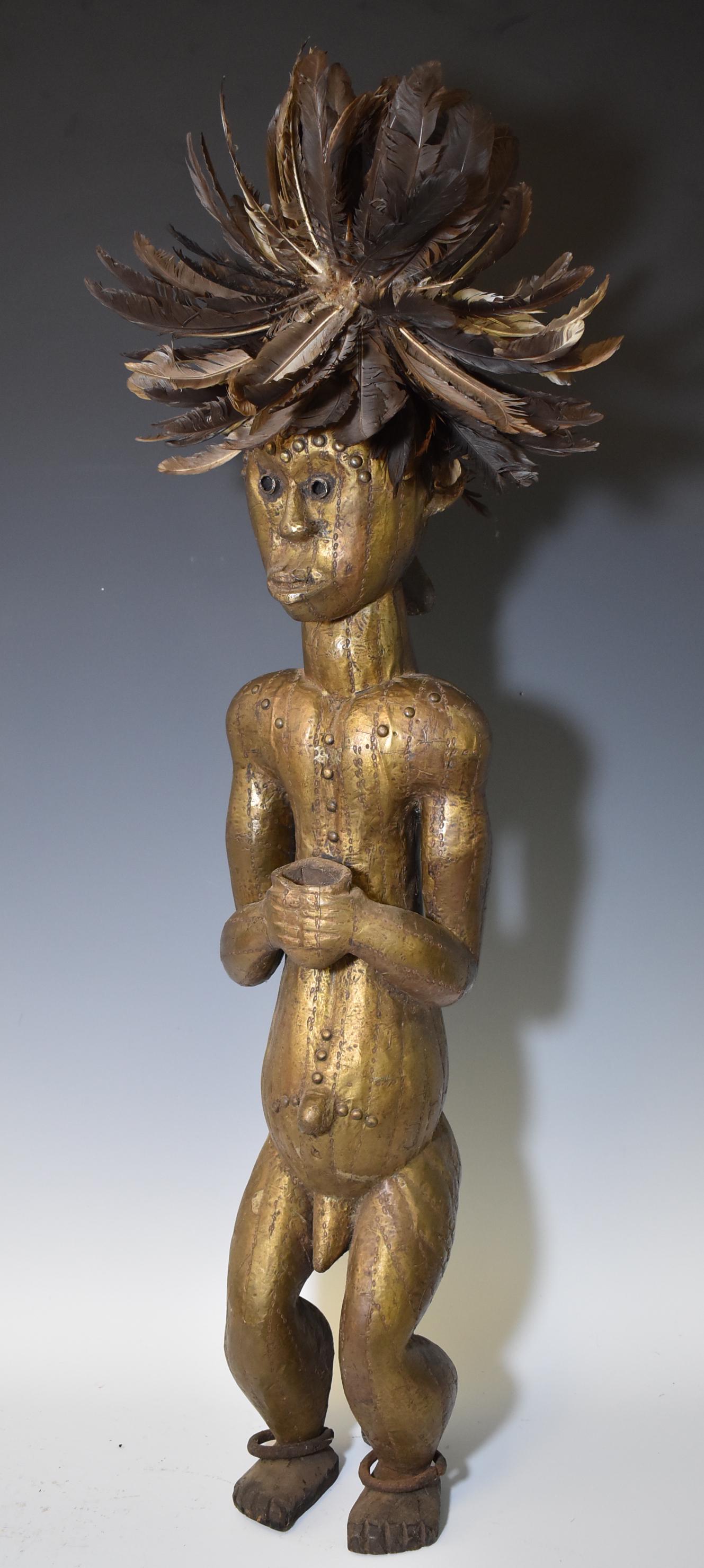 Rare Type Fang Bieri Figure: Highly uncommon. Completely metal clad; Except back of head. Male bone bundle figure holding a cup for offerings. Bronze anklets and feathered crown. Size 38"H to top of feathers.