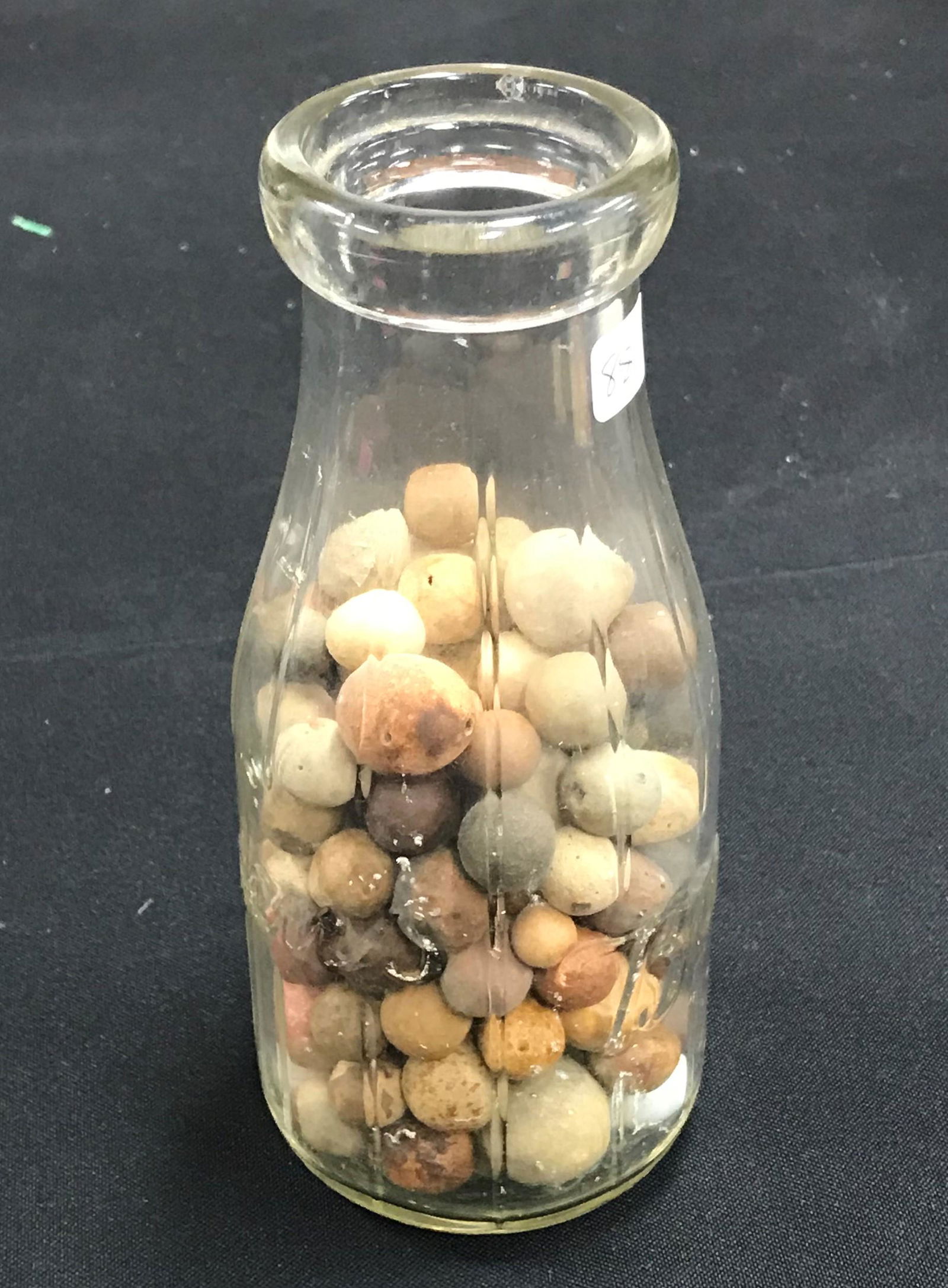 Antique Clay Marbles (130): Antique clay marbles, varying sizes, found over a period of years at a Beacon, New York playground (no longer there). Housed in a glass antique Borden's milk bottle. (9"H)