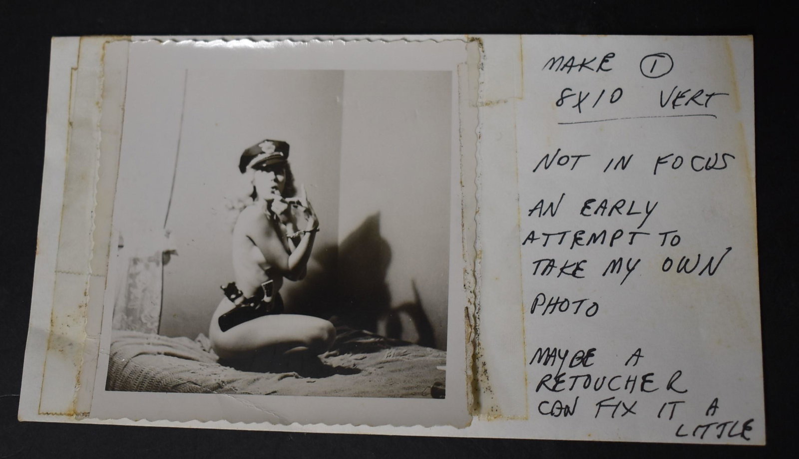 Bunny Yeager Early Self Portrait: With notations. "Make 8 x 10 vertical, Not in focus. An early attempt to take my own photo. Maybe a retoucher. Can fix it a little" in Bunny Yeager's hand. With pistol and holster and a cop's cap. Sma
