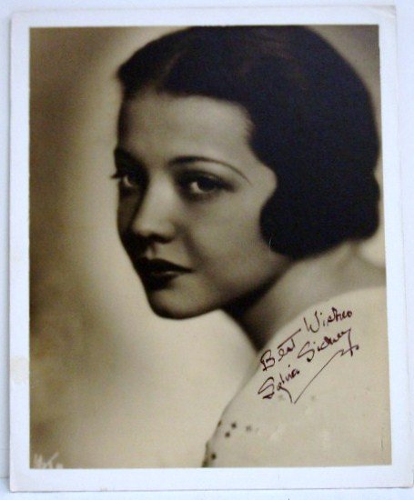 ISP SYLVIA SIDNEY: Best wishes Signed boldly in blue ink. Sylvia Sidney, Mounted on Bainbridge Board, Photographer's mark L. L. not discernible. 10 x 12 3/4 (Photo) 11 x14 (Overall) VF
