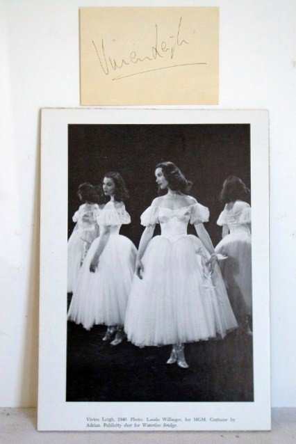 VIVIEN LEIGH AUTOGRAPH: In black ink on 3 x 4 manila card. Accompanied by photo of Ms. Leigh in a costume by Adrian. Publicity photo for MGM was shot by Willinger. Copy mounted on decorative board. 7 x 10.