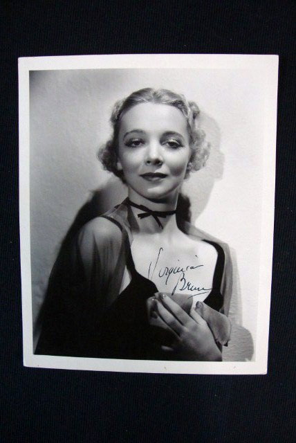 VIRGINIA BRUCE SIGNED PHOTOGRAPH: Signed in black ink Virginia Bruce. Backstamp for Hurrell & MGM, date stamp for July 11, 1940. Publicity snipe for The Great Ziegfeld. 8 x 10. VF