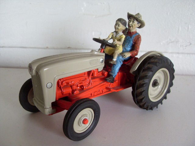 1953 FORD TRACTOR: Red & white Golden Jubilee Model Ford tractor. With farmer letting his daughter drive. Manufactured by Ertl. #'d 0247 on bottom. 7" long
