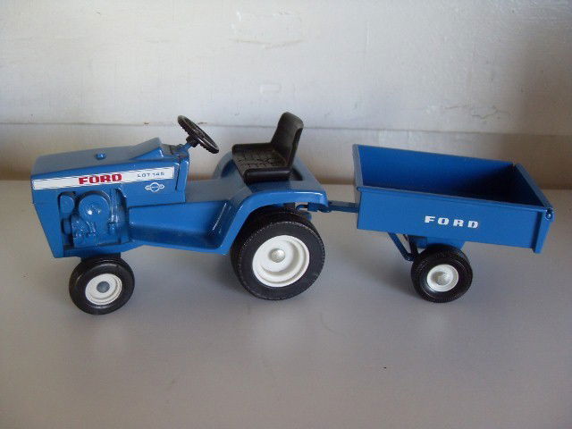 FORD LGT 145 TRACTOR AND CART: Blue Ford LGT 145 hydrostatic tractor with pull behind cart. Tractor is numbered 808 7203. Cart is numbered 815 211A. Manufactured by Ertl. Together tractor & cart are 11" long.