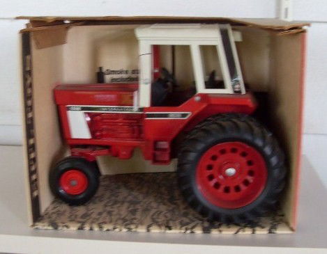 INTERNATIONAL 1586 TRACTOR WITH CAB: Red and white International 1586 tractor with cab. 1/16 scale. Die-cast metal. With smoke stack, rear hitch, and steerable front end. In original box. Manufactured by Ertl. Model #463. Numbered 3344.