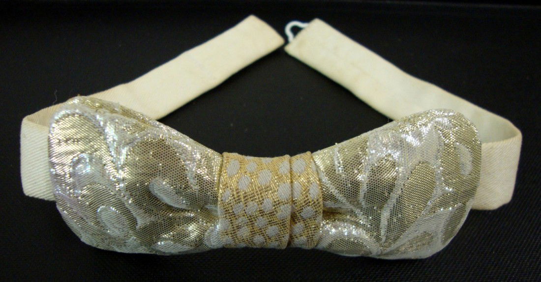 LIBERACE'S SILVER AND GOLD BOW TIE: In the 1940's Liberace handmade his bow ties. 15 1/2" overall length. Bow measures 2" X 4 1/2"-Gold polka dot center with silver leaf design.