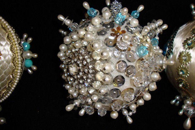 17 LIBERACE JEWELED CHRISTMAS ORNAMENTS: Four green satin covered holiday balls. Decorated with faux pearls, gold trim, golden angels and stylized flowers. five beaded and sequinned ornaments- holiday balls in blues and creams, silver and go