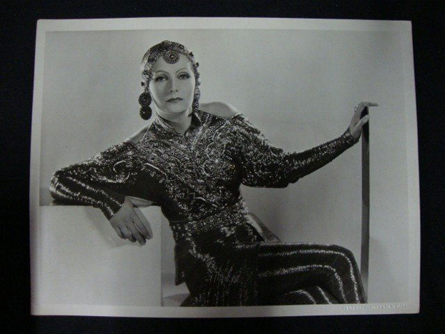 Clarence Sinclair Bull Photograph - Greta Garbo: Greta Garbo fashion portrait wearing an exotic dark, beaded, belted, open-shouldered tunic with leggings and a matching elaborate headpiece. On the reverse is a backstamp for the photographer, Clarenc