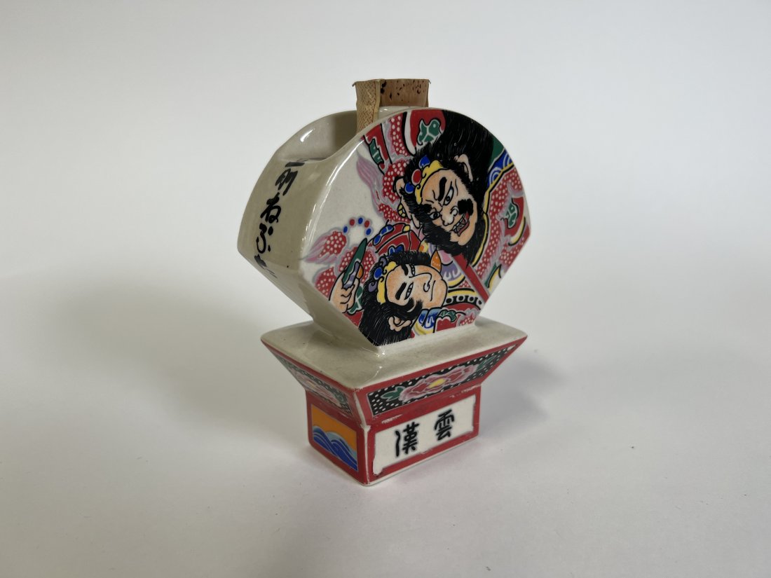 Oriental Whiskey Bottle. Sealed: Signed at the underside with initials of the artist S F 4"H and wide. Original label at front ( In Chinese characters). Depicts Samurais at one side Geisha with sword and shield at the other side with