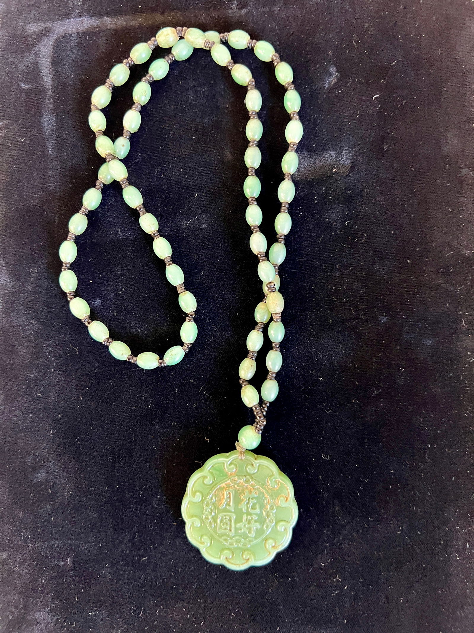 Emerald/Jadeite Burma Necklace: Emerald green beads with pendant, a fine translucent stone, the pectoralis carved in calligraphy, probably a reign mark. Silk knotted. Picture not accurate as to color, deep green patina to both penda