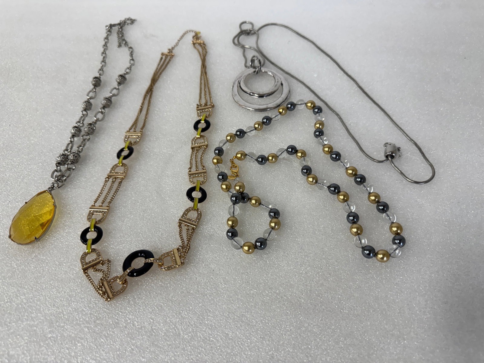 Collector or Dealer's Lot of Costume Necklaces (4): Modernist 50's silverplate necklace; large faceted amber pendant on an openlink silverplated chain; a sgd.Mark goldplated and yellow and black enameled long chain +or belt; a marked Joan Rivers gold a