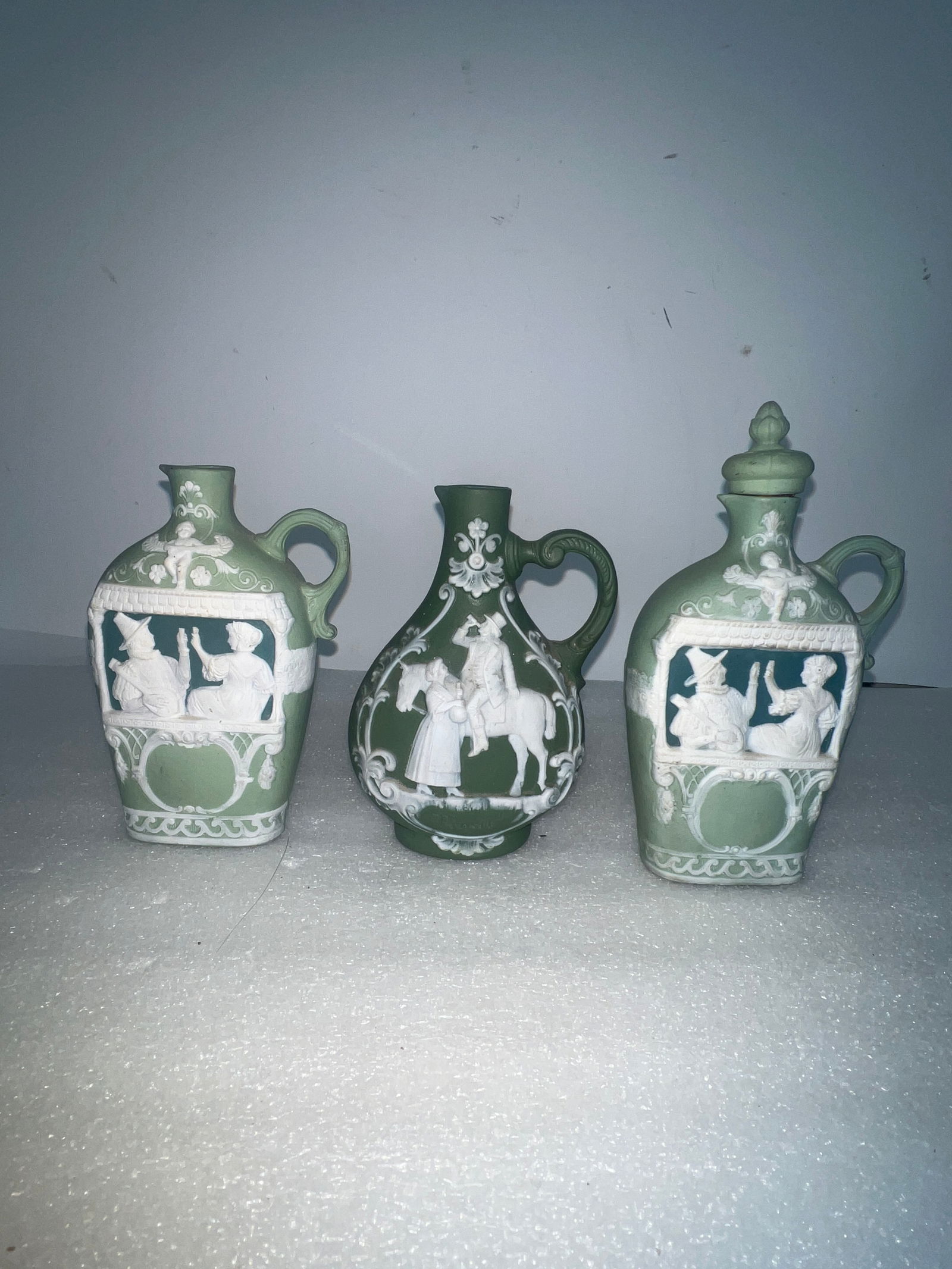 Green Wedgwood Type Antique Pitchers.: As pictured. One with a lid, two without. With lid is 6.5”H. The two without are 5.25”H.