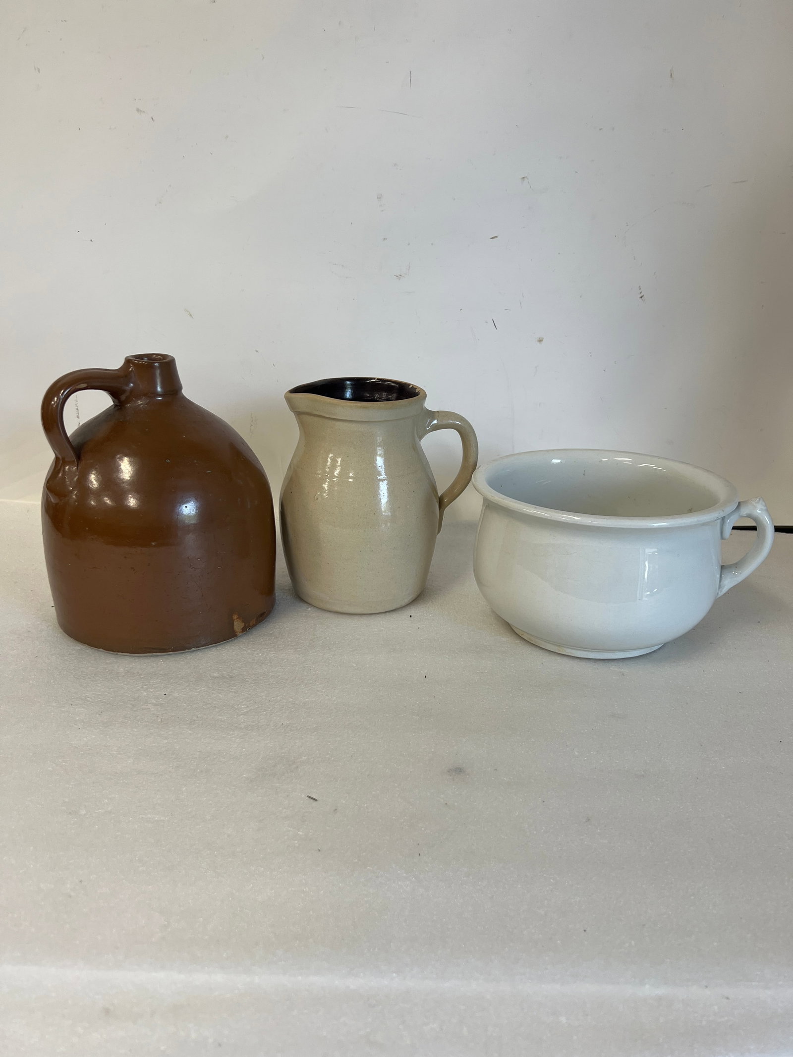 Dealer or Collector's Lot of Stoneware (3): Included in the lot is an ironstone white chamber pot (5.5”H by 9” in diameter”; a stoneware pitcher (8.25”H)and a brown handled antique jug. Three in the lot. (9.75”H)