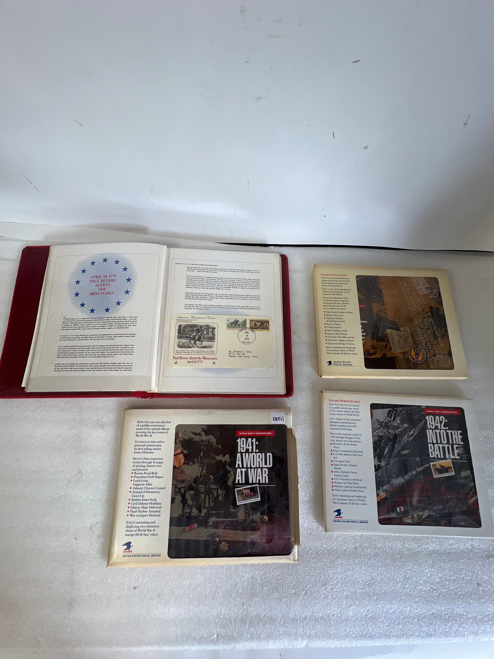 Lot of WWII Stamp Albums (4): Three albums contain a 40-page book detailing 1941 events like Pearl Harbor and the Lend-Lease Act. The other is a red leatherette binder, embossed with gold lettering and a Liberty Bell emblem,