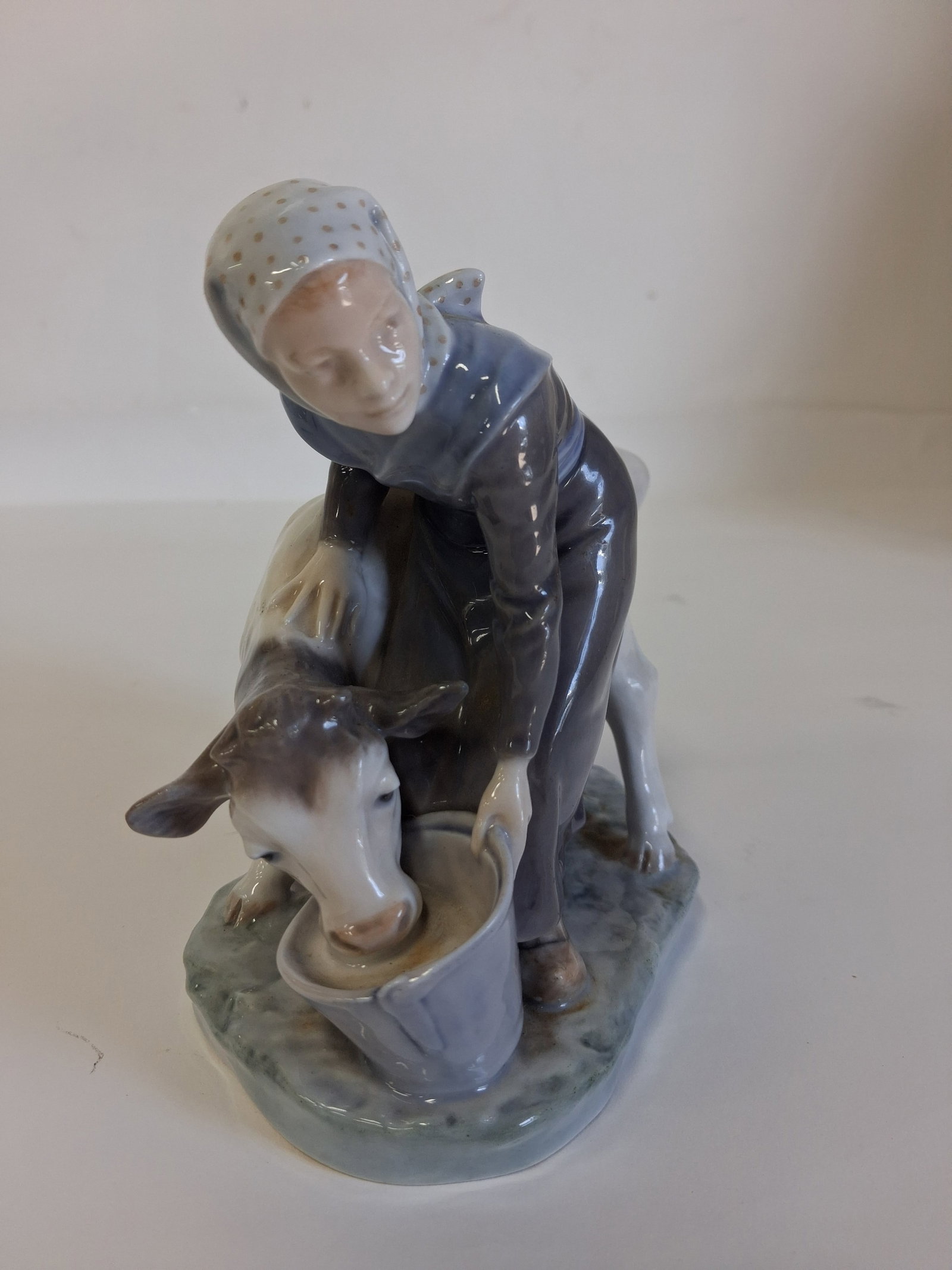 Royal Copenhagen Porcelain Figure.: Girl Feeding a cow. With Royal Copenhagen markings at the underside6in H x 6in W