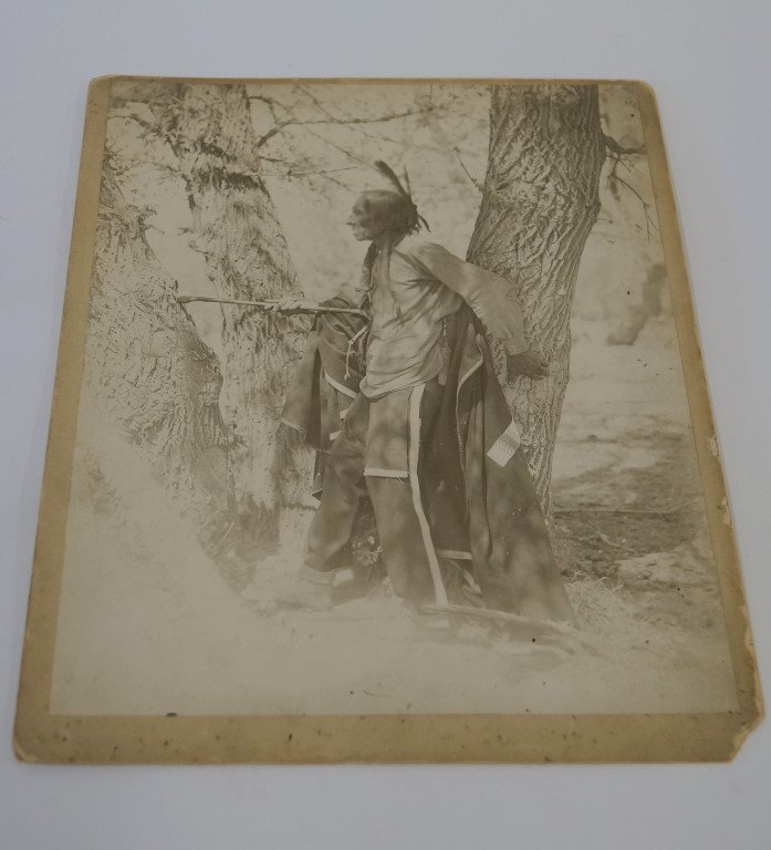 Photograph Elderly Indian Warrior: Full profile, holding a tomahawk. Otter skin and feather hair ornaments. Collection photograph on slightly larger mount. Possibly photographed by Heyn. C 1898. 11x14"