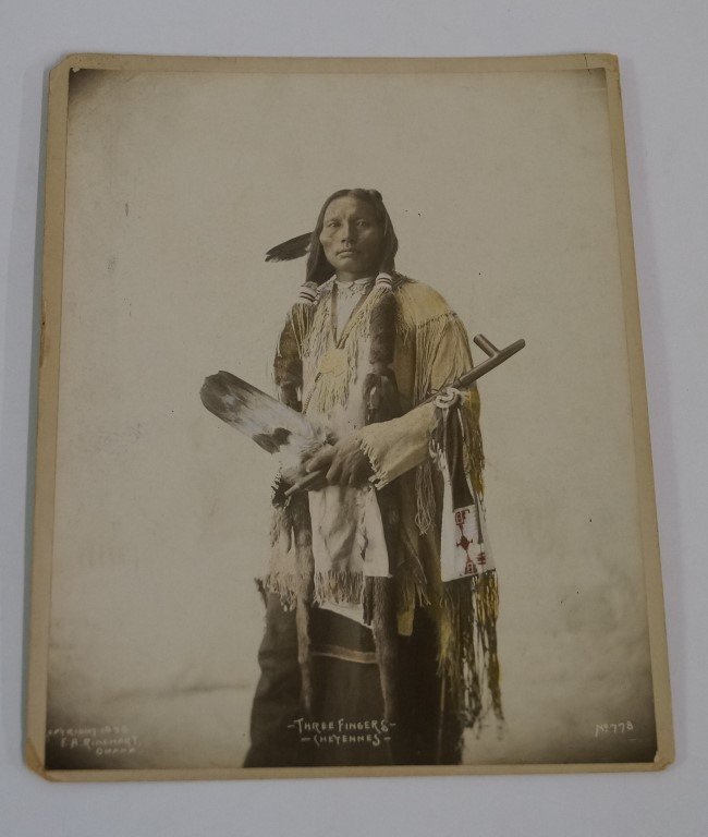 "Three Fingers " of the Cheyenne Tribe: Original 8x10" tinted album of a proud warrior, nearly full standing view, single feather in hair, fur covers over his long braids. He holds a long pipe across his body, with beaded pouch and large fe