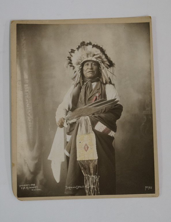 "Turning Eagle "of the Sioux Tribe: Original 8x10" album photograph of Indian wearing full head-dress, wrapped in a blanket and holding three or four huge feathers across his body. Beaded bag, lightly tinted, flows down from the middle 