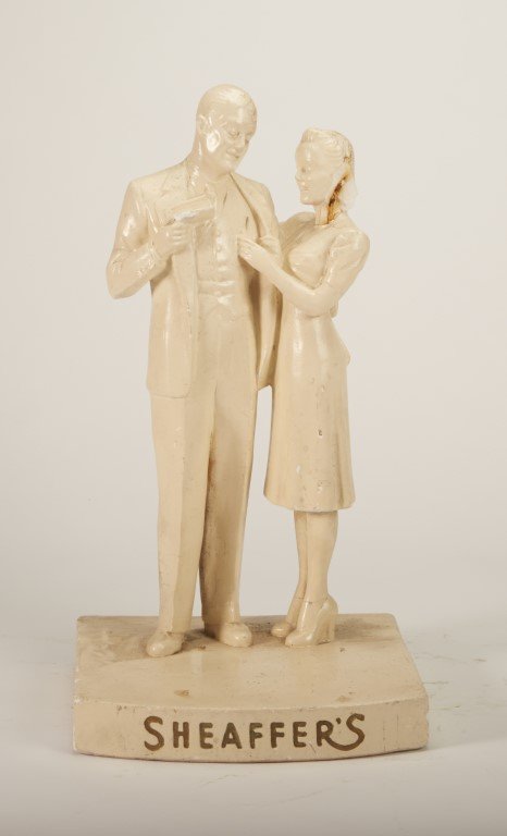Sheaffer's Figural Couple: Depicts couple sharing Sheaffer's pens. Plaster and glaze. Condition: Some small chips, and one large chip on woman's hair.; 15" x 8"