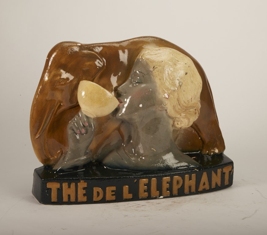 The De l'Elephant Display Piece: Painted plaster. Depicts woman drinking tea cup with elephant in background. Minor paint chipping. ; 11 1/2" x 14 1/2"