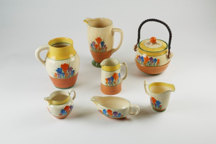 Clarice Cliff Bizarre Line: Crocus ( 7 pcs.): 8" Pitcher. 8" Pitcher. Gravy Boat 2 1/4". Handled Jar 6". Creamer 5". Saucer 4". Saucer 3". ( 7 pcs. in the lot.)
