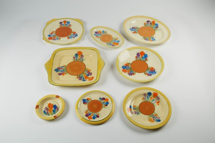 Clarice Cliff Bizarre Line: Crocus (21 pcs.): One Ashtray 5". One Trivet 6 1/2". 8 Plates 8". 3 Plates 9". 2 Plates 9". One Platter 10 1/2". One Platter 8 1/4". One Plate 11 3/4". 2 Serving Plates 11 1/4". One Plate 10". (Approx. 21 pcs. in the l