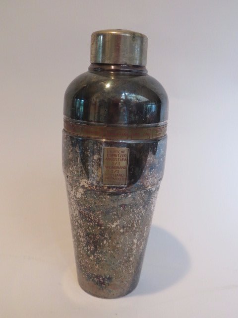 DRGM German Cocktail Shaker: With names of drinks in panels in a band surround inc. Side Car, Manhattan , White Lady, Bronx, Between the Sheets, Ohio, etc. Rotating collar has a window revealing ingredients for the various drinks