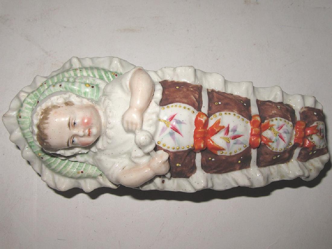 Rare Staffordshire Box. Baby in Bed: Rare Staffordshire box, a baby with rattle and in bonnet in a fancy "bed" covered by a beribboned fancy blanket with ruffles, bows and placques decorated with leaves. Unidentified mark which looks lik