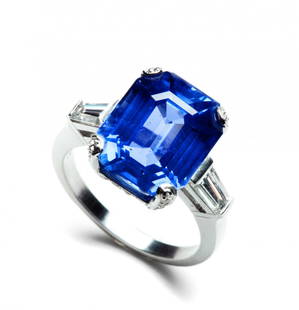 An impressive platinum Burma sapphire ring, set with an: An impressive platinum Burma sapphire ring, set with an emerald-cut sapphire weighing approximately 11.50 carats, between two step-cut diamond weighing approximately 0.30 carats. Assay marks. Weight