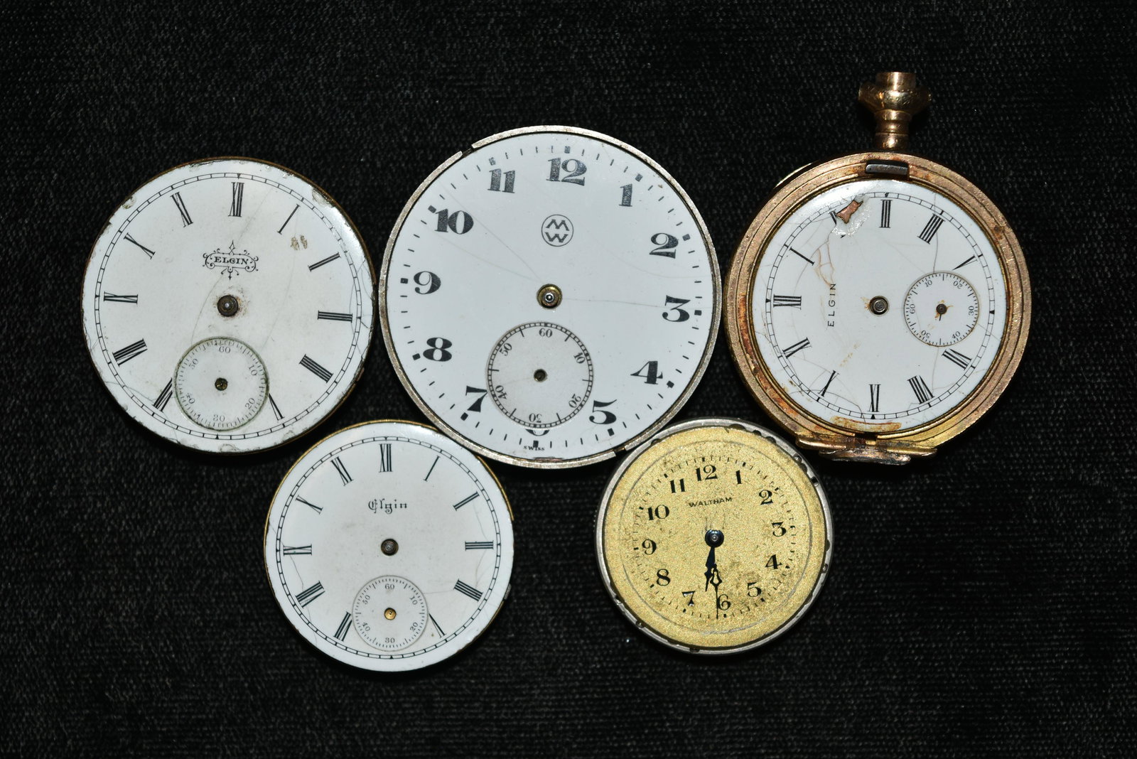 Box lot of five antique pocket watch works. Porcelain: Box lot of five antique pocket watch works. Porcelain and metal dials. Largest is 1 1/2" . Faces marked Elgin, Waltham. On back of works marked Frizt Moeri, Switzerland