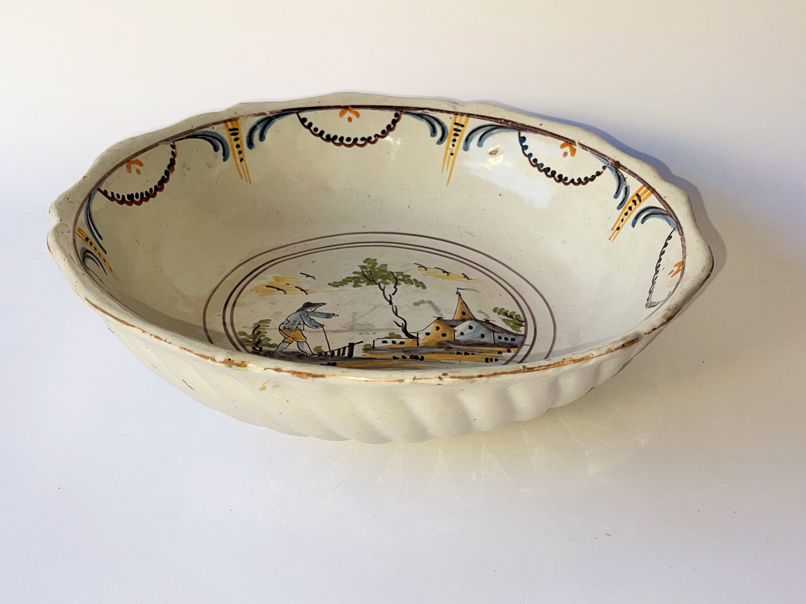 18tTH CENTURY NEVERS FAIENCE TIN GLAZE BOWL: 18TH CENTURY NEVERS FAIENCE TIN GLAZE BOWL. Fluted sides; hand painted images, scalloped rim. Hanging holes on foot. Unmarked. Diameter 12 ½”. A few small chips to rim and one to undersid