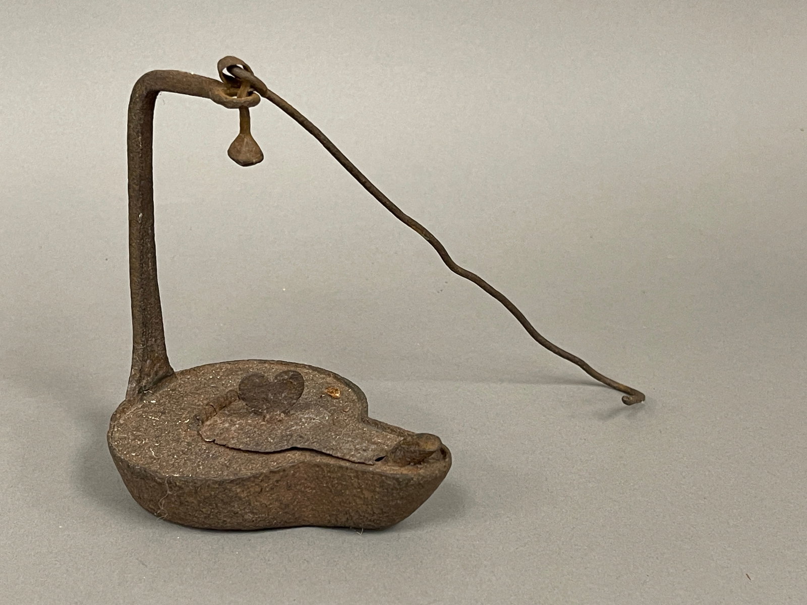 IRON HINGED LID BETTY LAMP WITH HEART FINIAL: ANTIQUE IRON HINGED LID BETTY LAMP WITH HEART FINIAL. 4 ¼” X 5” TALL X 3” WIDE. GOOD CONDITION.