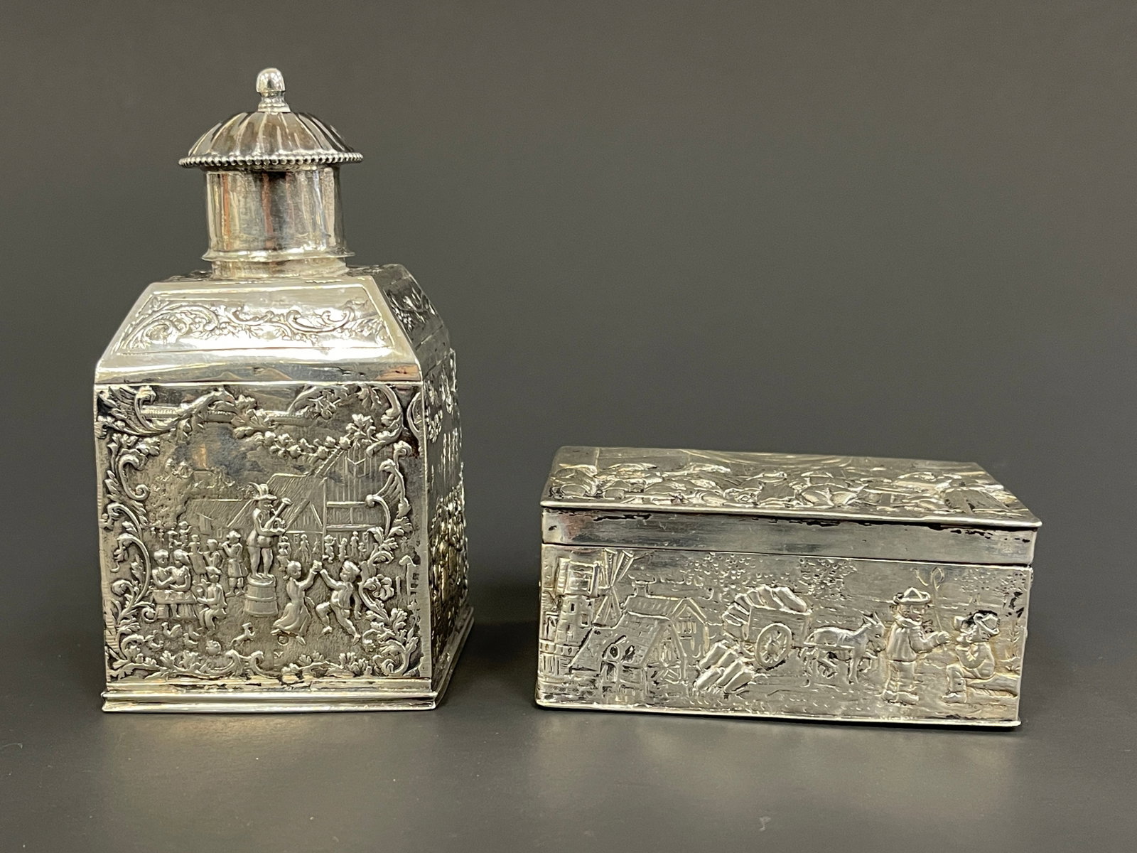 TWO SILVER REPOUSSE CADDIES DEPICTING VILLAGE SCENES (1 of 6)