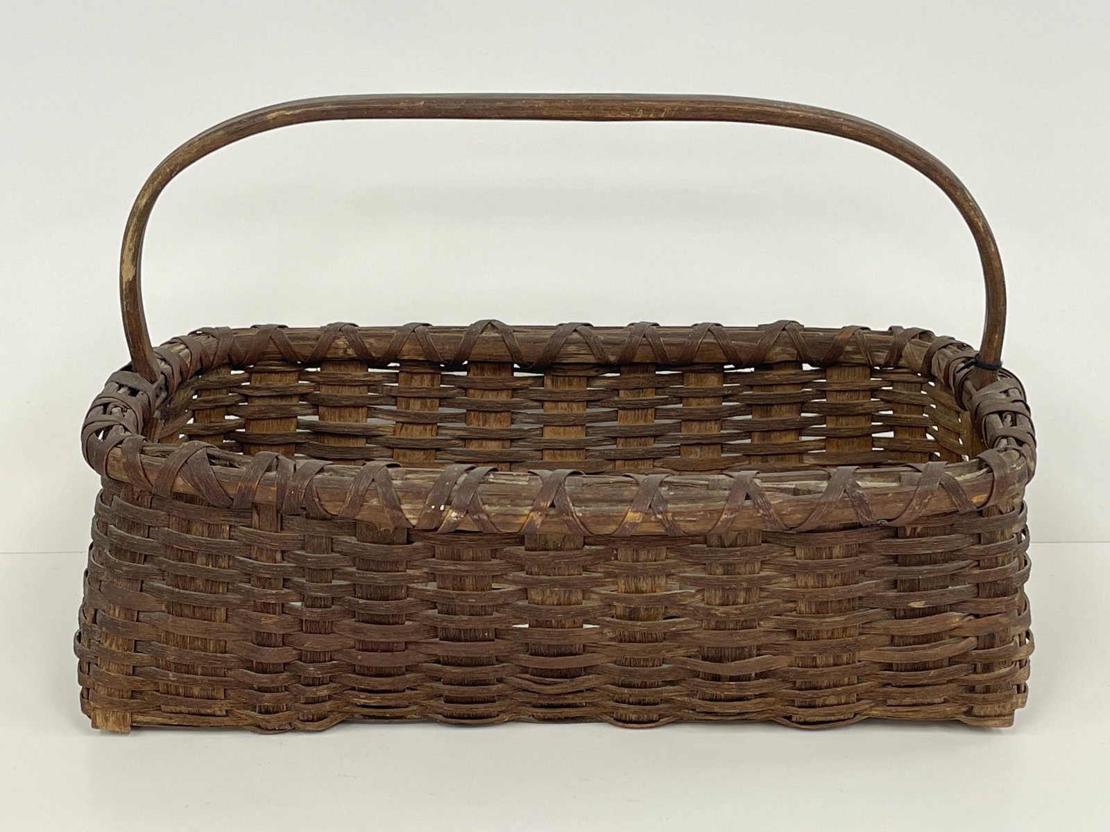19TH C SHAKER RECTANGULAR UTILITY BASKET: 19TH C SHAKER RECTANGULAR UTILITY BASKET WITH LONGWISE HANDLE, LIKELY CANTERBURY, NH. THE HANDLE WAS NOT FORMED ON A MOLD. IT IS CARVED OUT AND BENT TO SHAPE. THE TAILS GO DOWN INTO THE BOTTOM AND